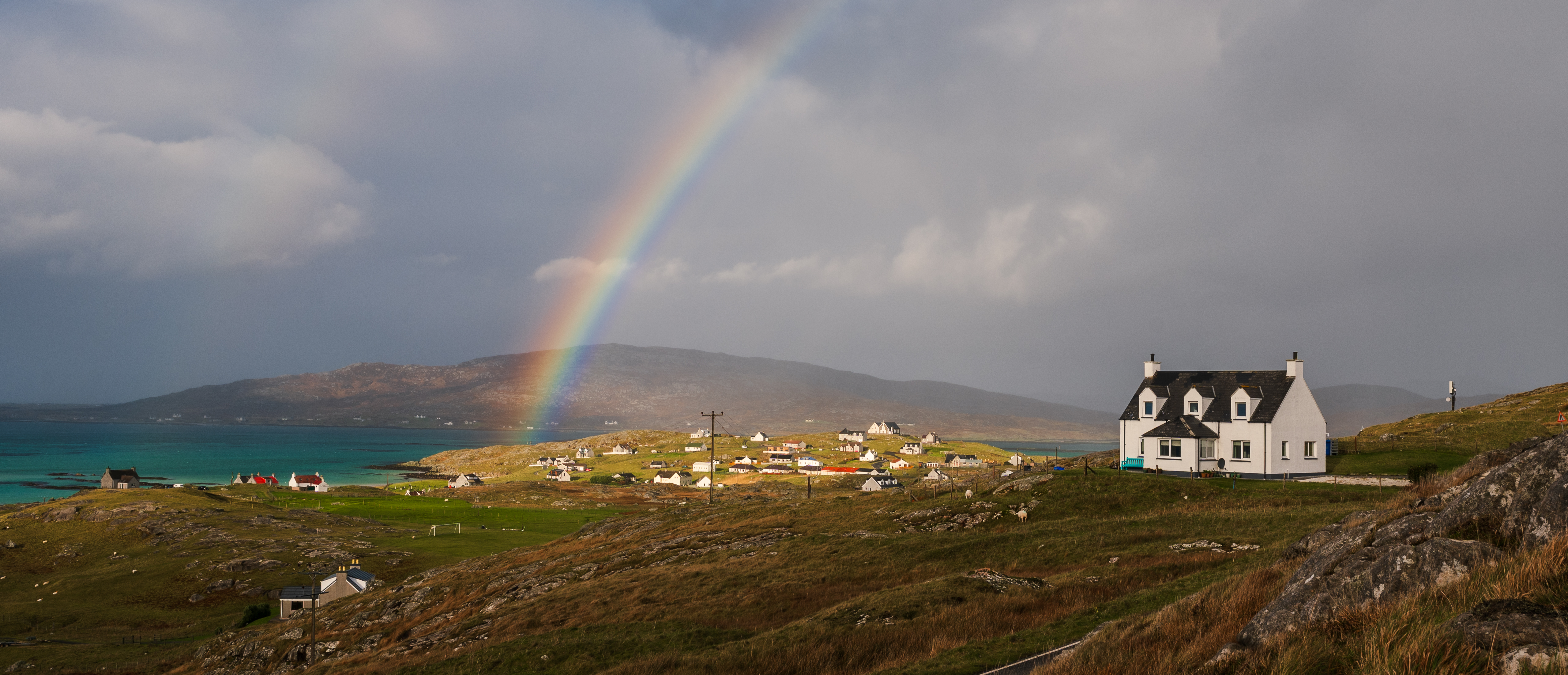 White house on a hillside above the Scottish coast under a rainbow